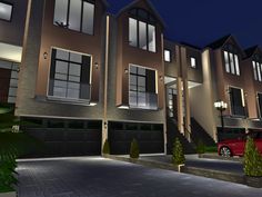 a red car is parked in front of two story townhouses at night with lights on