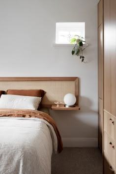 a bed sitting next to a wooden dresser under a window with a potted plant on top of it