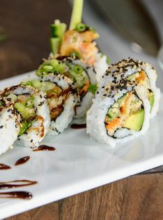 sushi on a white plate with sauce drizzled over it and garnished with sesame seeds