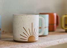 three coffee mugs sitting on top of a shelf next to each other in different colors