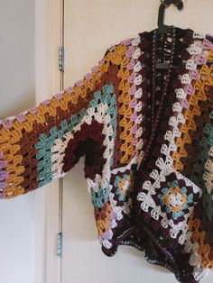 a colorful crocheted sweater hanging on a door hanger in front of a white door