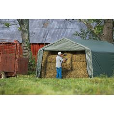 a man standing next to a hay bale in front of a red barn with a green tarp on it