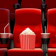 an empty red cinema seat with popcorn and drink in it, next to two soda cups