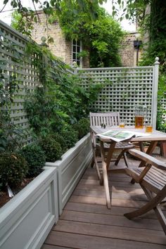 there is a table and two chairs on the deck in front of some bushes,