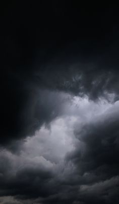 an airplane is flying in the cloudy sky with dark clouds behind it and another plane on the ground