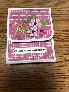 a pink card with flowers on it sitting on top of a wooden table next to a pen