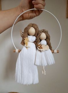 two dolls are hanging from a hoop with tassels on the end and one is holding another doll