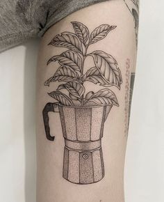 a black and white photo of a plant in a coffee cup tattoo on the arm