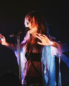 a woman standing in front of a microphone and holding her hand out to the side