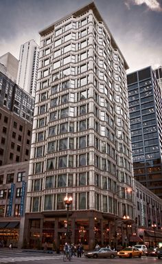 a tall building sitting in the middle of a street next to tall buildings with windows