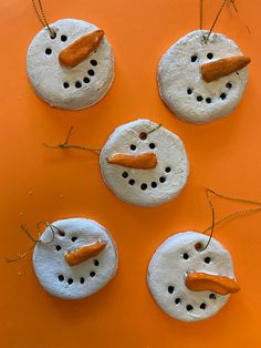 four snowmen made out of clay sitting on top of an orange surface with string