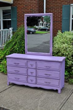 a purple dresser with a large mirror on it's top and bottom drawers in front of a brick building