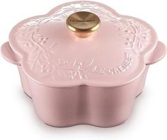 a pink casserole dish with a gold lid and flower design on the side