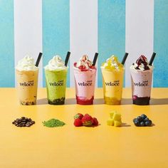 five different flavored drinks are lined up on a yellow table with blue and white striped walls