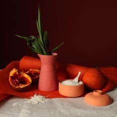 there is a pink vase with some food in it and two oranges on the table