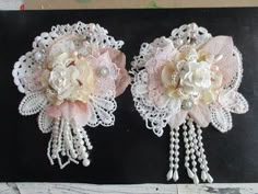 two pink and white flowers are on a black board with pearls hanging from it's sides