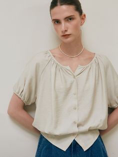 a woman standing in front of a white wall with her hands on her hips wearing a necklace