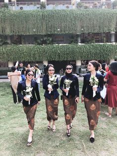 three women are walking through the grass with flowers in their hair and wearing matching outfits