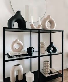 a shelf with vases and books on it in front of a wall mounted mirror