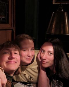 three people sitting at a table with wine glasses in front of them and a lamp on the wall behind them