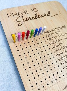 a wooden board with several colored pegs on it that says phase 10 scoreboard