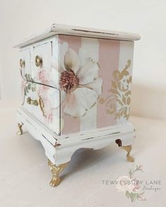 a white and pink chest with flowers painted on the front, sitting on a table