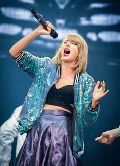 a woman holding a microphone up to her head and singing into the air with both hands