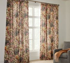 a living room filled with furniture and a window covered in floral drapes next to a chair