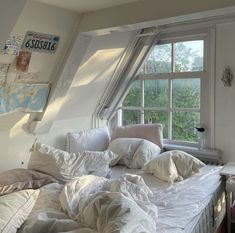 an unmade bed sitting in front of a window with lots of pillows on it