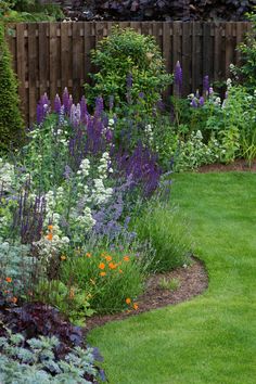 a garden filled with lots of different types of flowers and plants next to a wooden fence