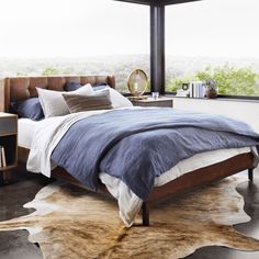 a bedroom with a bed, nightstands and large windows overlooking the cityscape