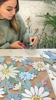 a woman sitting at a table with flowers painted on the board and scissors in her hands