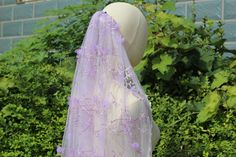 a veil with purple flowers on it is sitting in front of bushes and shrubbery