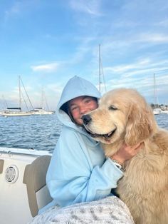 a woman in a blue hoodie holding a dog on the back of a boat