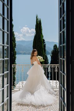 a woman in a wedding dress is standing by an open door looking at the water