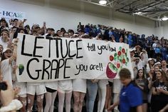 a group of people holding up a sign that says lettuce grape you're