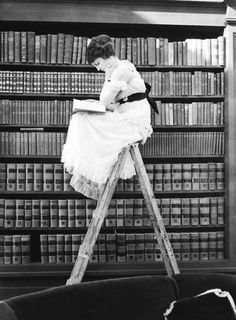 a woman sitting on top of a ladder in front of a bookshelf