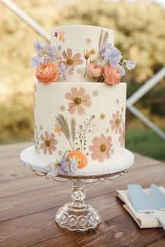 a white cake with flowers on it sitting on top of a wooden table next to napkins