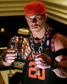 a man wearing a red hat and chain around his neck holding a wrestling belt in front of him