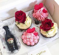 four cupcakes in a box with roses on them and a bottle of booze