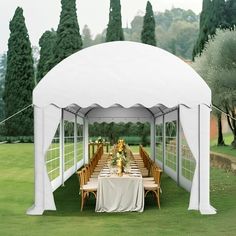 a table set up under a white tent for an outdoor dinner or party with greenery and trees in the background