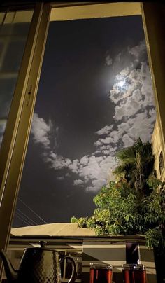 an open window shows the night sky with clouds and trees in it, as well as coffee mugs