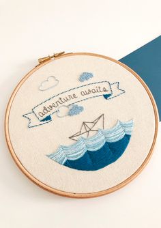 an embroidery project with the words adventure awaits and a paper boat floating in the ocean