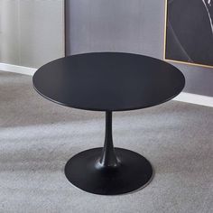 a round black table sitting on top of a carpeted floor next to a painting