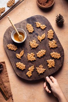 a wooden cutting board topped with cut out leaves next to a bowl of honey and spoon