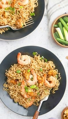 two black plates with shrimp and noodles on them next to green beans, as well as a fork