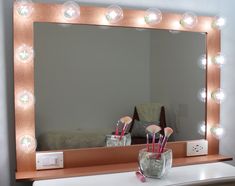 a vanity mirror with lights on top of it next to a vase filled with flowers