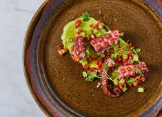 an octopus dish on a brown plate with green garnish and red pepper sprinkles