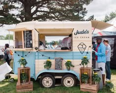 an ice cream truck is parked in the grass with people standing around and looking at it