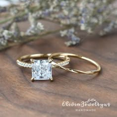 a gold ring with a princess cut diamond in the center on top of a wooden surface